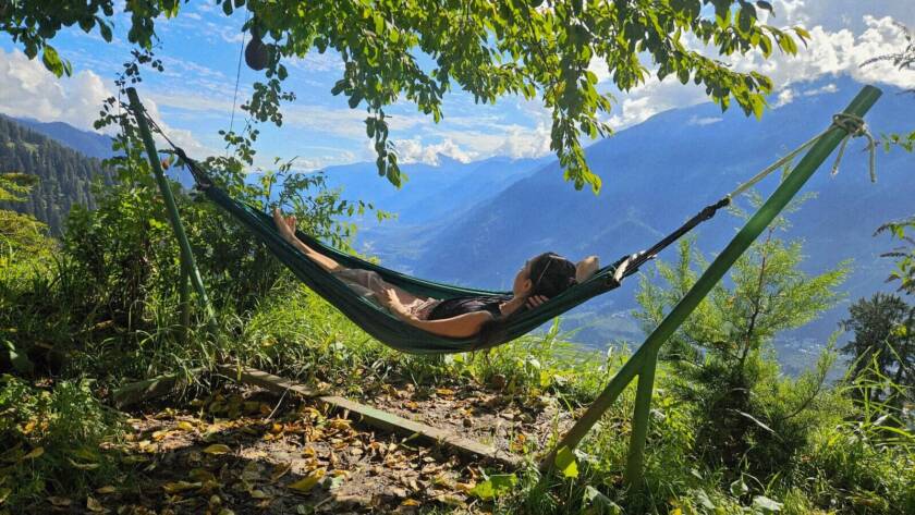 Solo female traveler relaxing in a hammock with Himalayan mountain views at GlampEco Manali