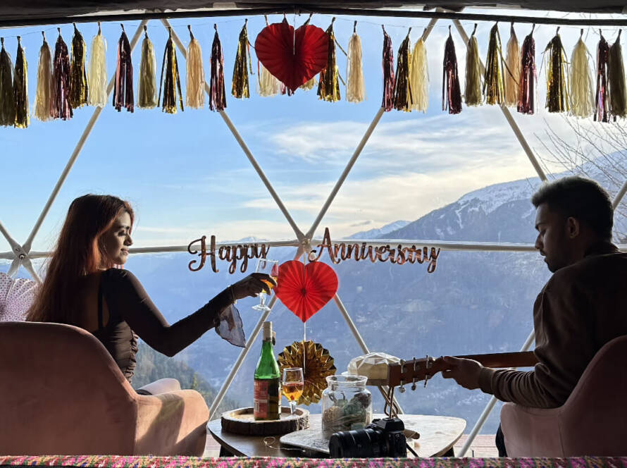 Couple celebrating their anniversary with romantic dome setup – cake and wine at GlampEco Manali